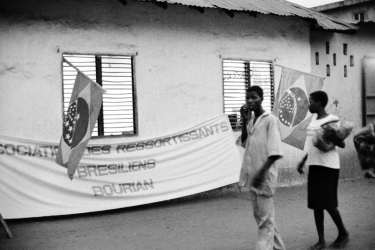 Casa da família Amaral. Preparação para o desfile de véspera da missa de celebração do N. S. do Bonfim. Na faixa esta escrito "Association des Ressortissants Brésiliens - BOURIAN", corruptela de 'burrinha'. - 21 de janeiro de 1995 - Porto Novo, Benim
