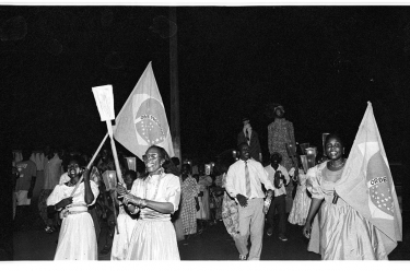 Desfile na véspera da missa do Bonfim. No primeiro plano, a sra. Amégan, née Campos, e as porta-bandeiras Evélyne Mariano, a esquerda, e Antoinette Campos. Ao fundo, com um pandeiro, Jean Amaral. - 20 de janeiro de 1996 - Porto Novo, Benim